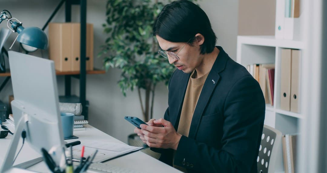 A man sitting at a desk using a cell phone