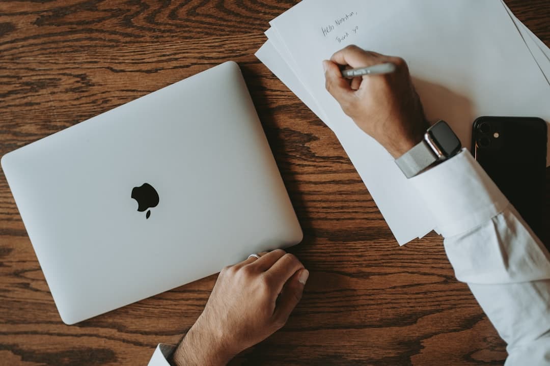 a person writing on a piece of paper next to a laptop