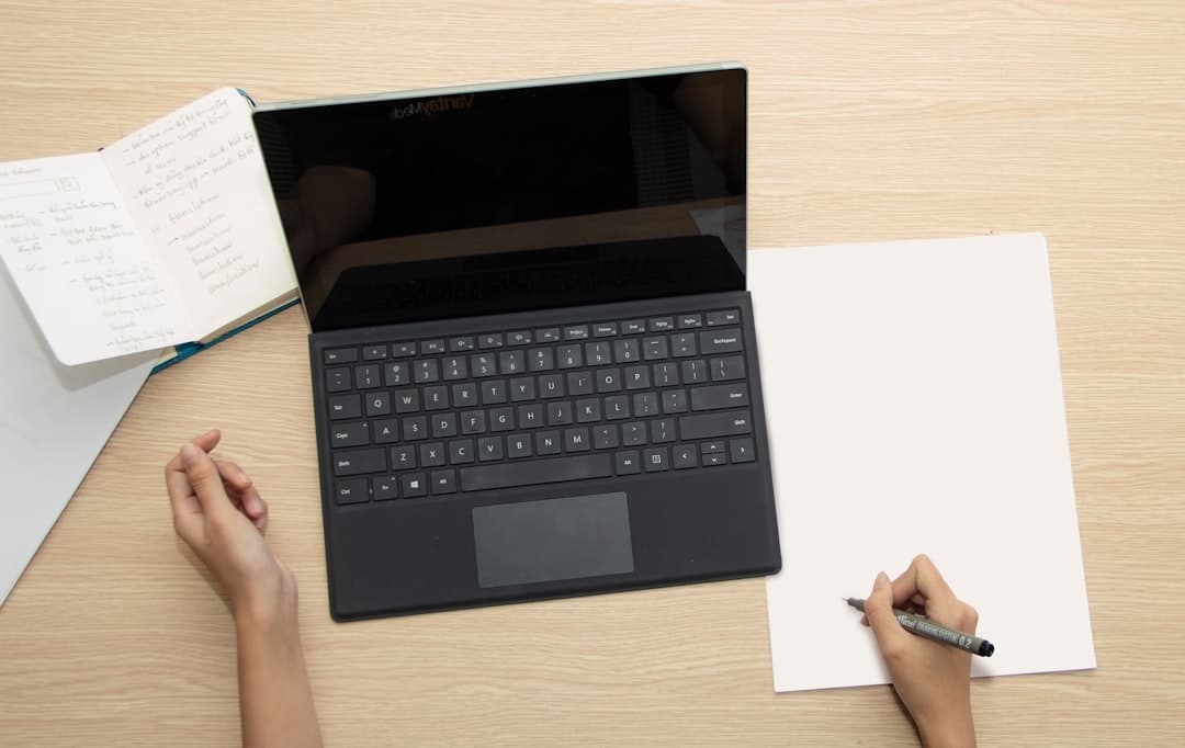 a person writing on a piece of paper next to a laptop