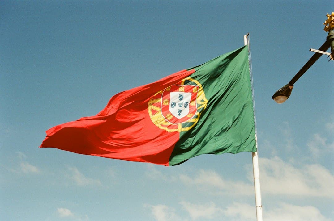 The flag of Portugal waving against a clear blue sky with a street lamp nearby