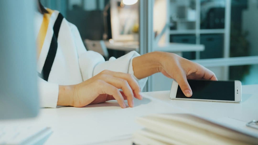 A person in a white sweater placing a smartphone on a white desk