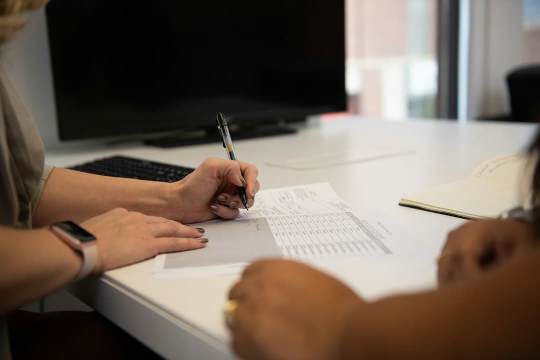 two people sitting at a desk writing on a piece of paper