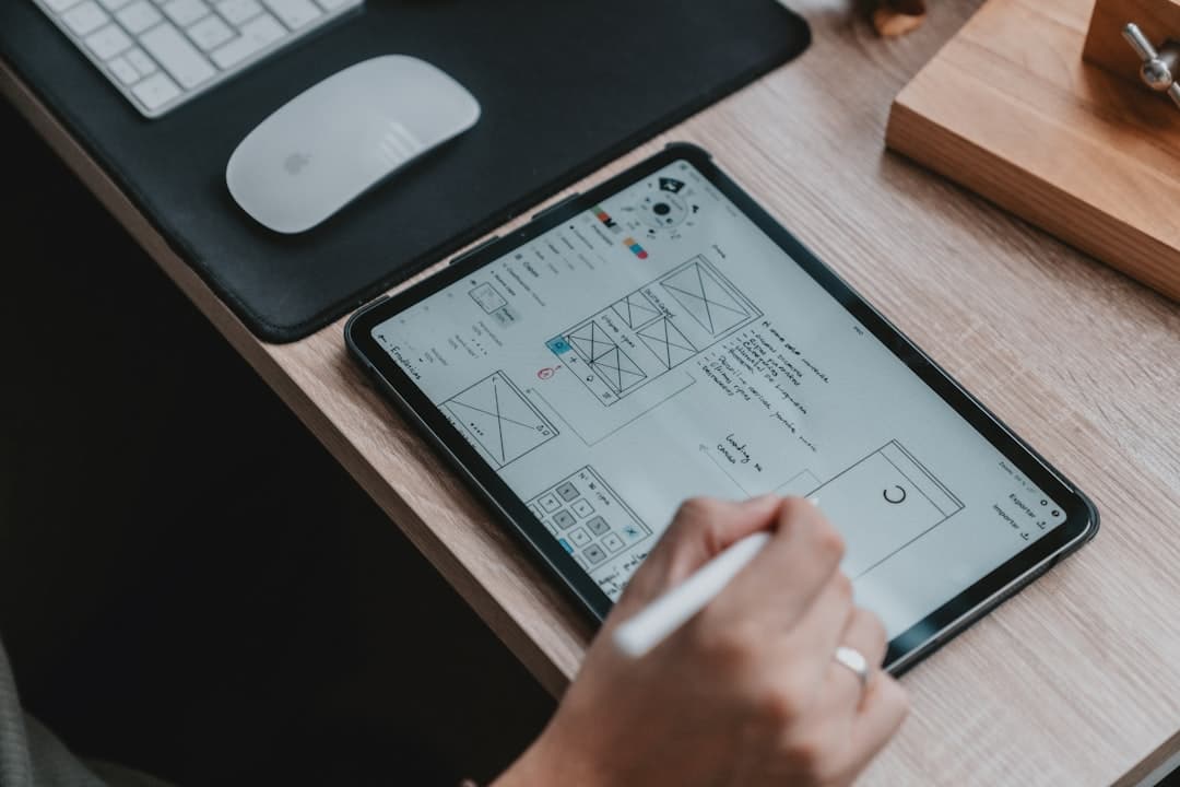 A person using a stylus on a tablet displaying wireframe sketches on a wooden desk